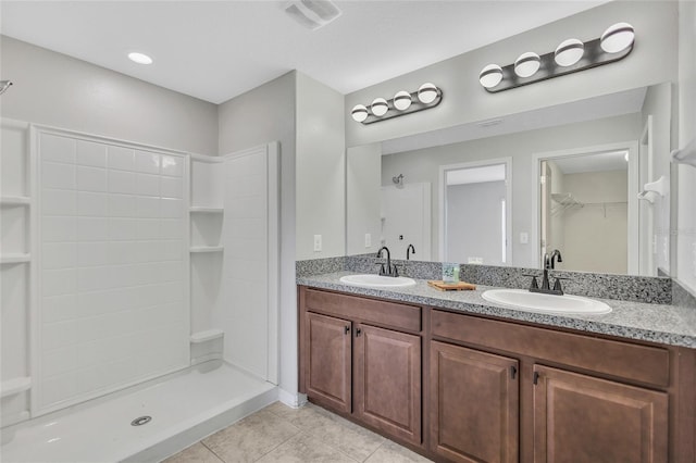 bathroom featuring a stall shower, double vanity, a sink, and tile patterned flooring