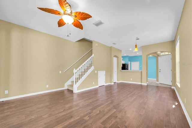 unfurnished living room with arched walkways, wood finished floors, stairs, visible vents, and a ceiling fan
