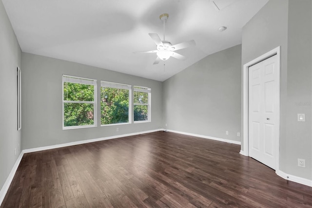 spare room featuring lofted ceiling, dark wood-type flooring, a ceiling fan, and baseboards