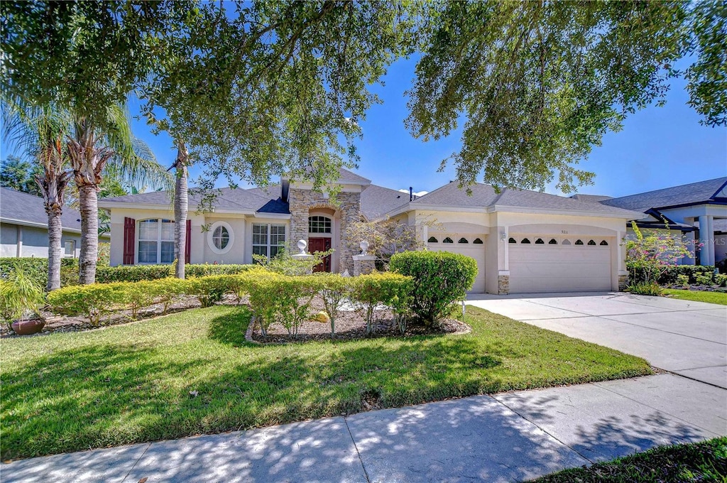 single story home with driveway, stone siding, an attached garage, a front yard, and stucco siding