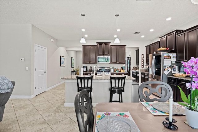 21383 Southern Charm Dr, Land O Lakes, FL 34637 - kitchen with light tile patterned floors, dark brown cabinets, visible vents, appliances with stainless steel finishes, and a center island with sink