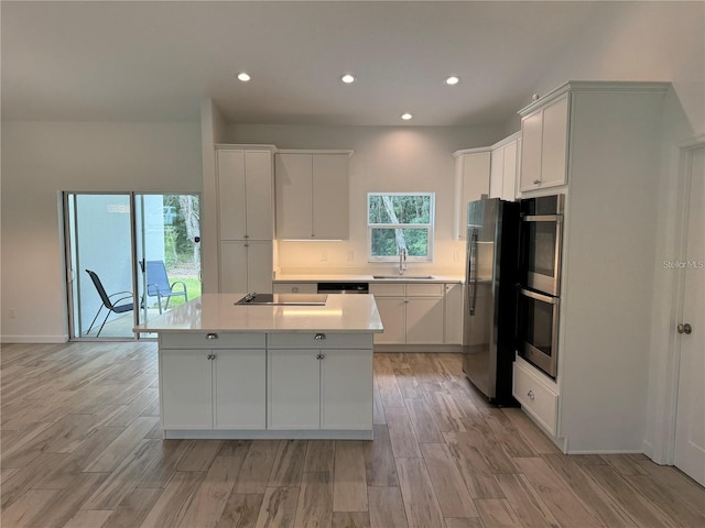 kitchen with light wood-type flooring, light countertops, a center island, stainless steel appliances, and a sink
