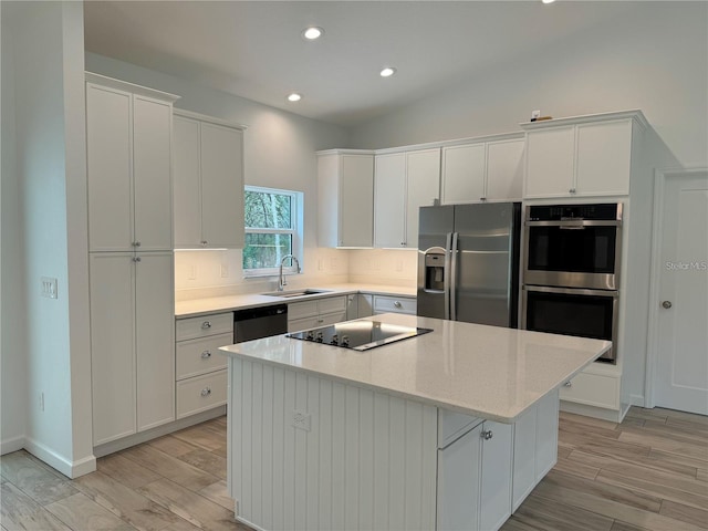 kitchen featuring light wood-type flooring, a center island, white cabinetry, stainless steel appliances, and a sink
