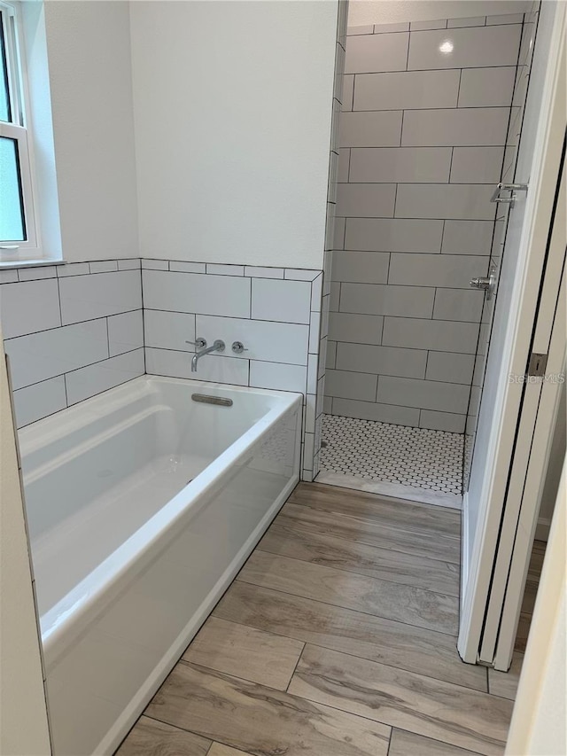 bathroom with a bath, a shower stall, and wood finished floors