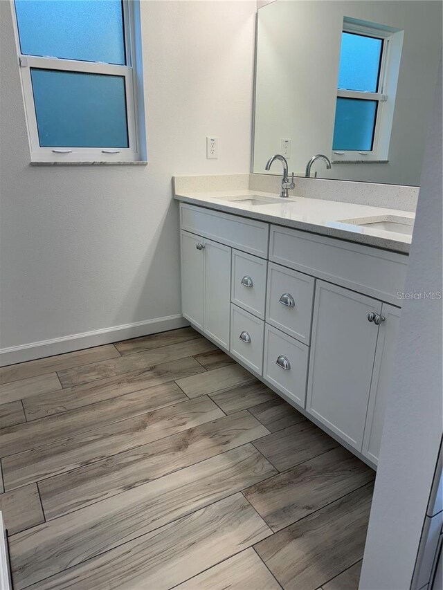 full bath with double vanity, baseboards, a sink, and wood finished floors