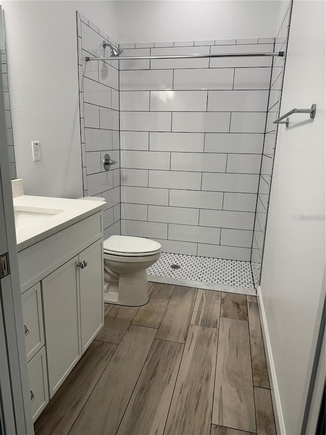 bathroom with toilet, tiled shower, vanity, and wood finished floors