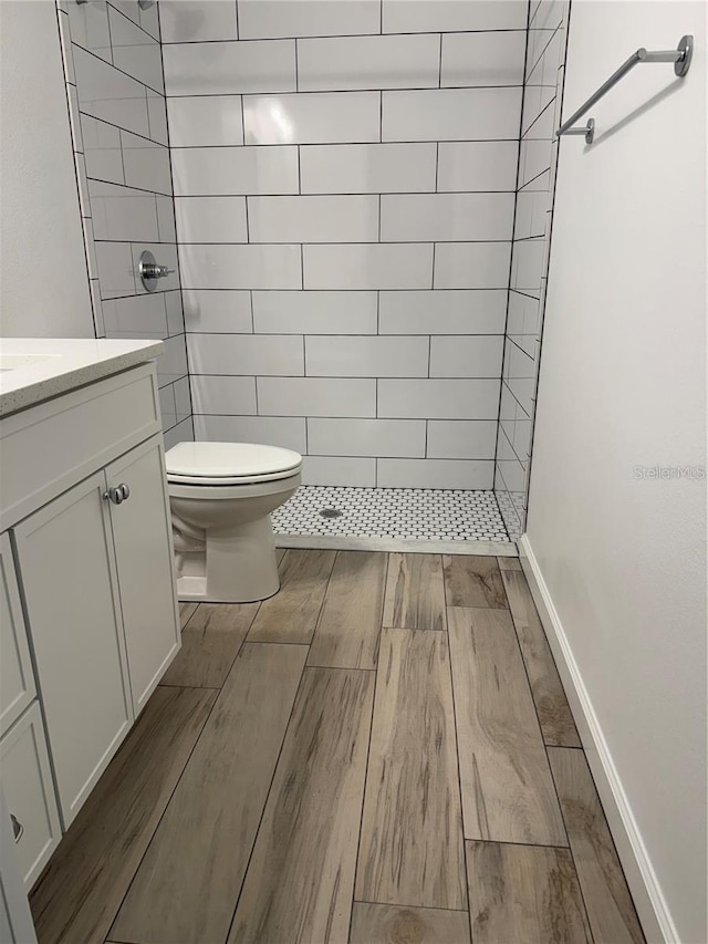 bathroom featuring a tile shower, wood finished floors, vanity, and toilet