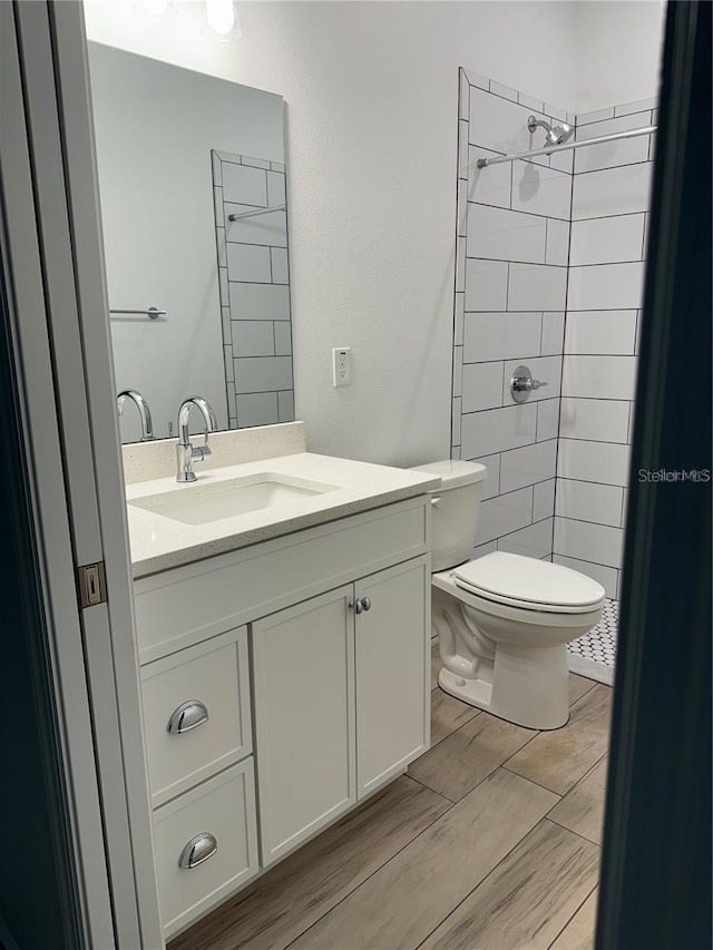 full bath with tiled shower, vanity, toilet, and wood finished floors