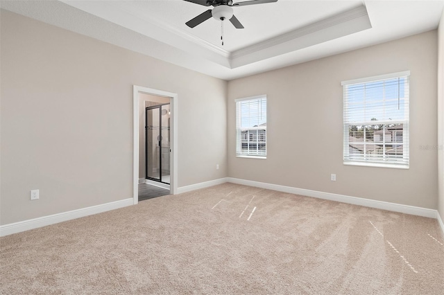 spare room with a tray ceiling, light colored carpet, a ceiling fan, ornamental molding, and baseboards