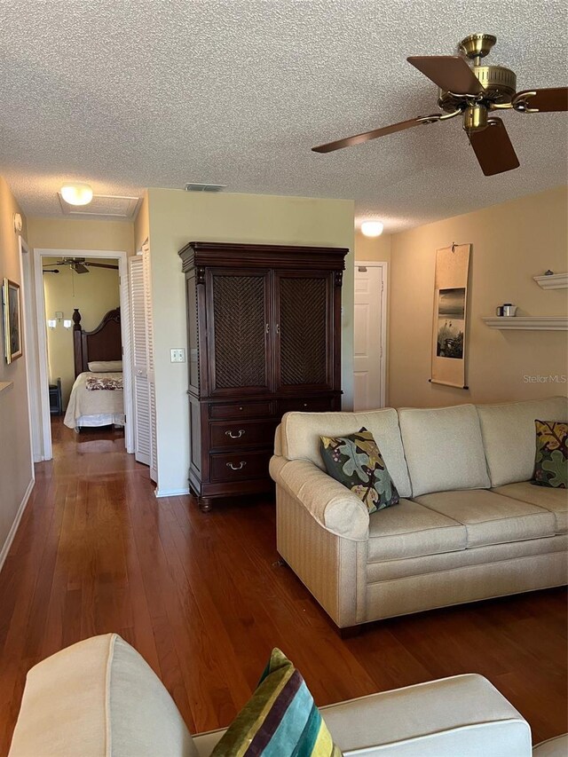 living area featuring a textured ceiling, baseboards, dark wood finished floors, ceiling fan, and visible vents