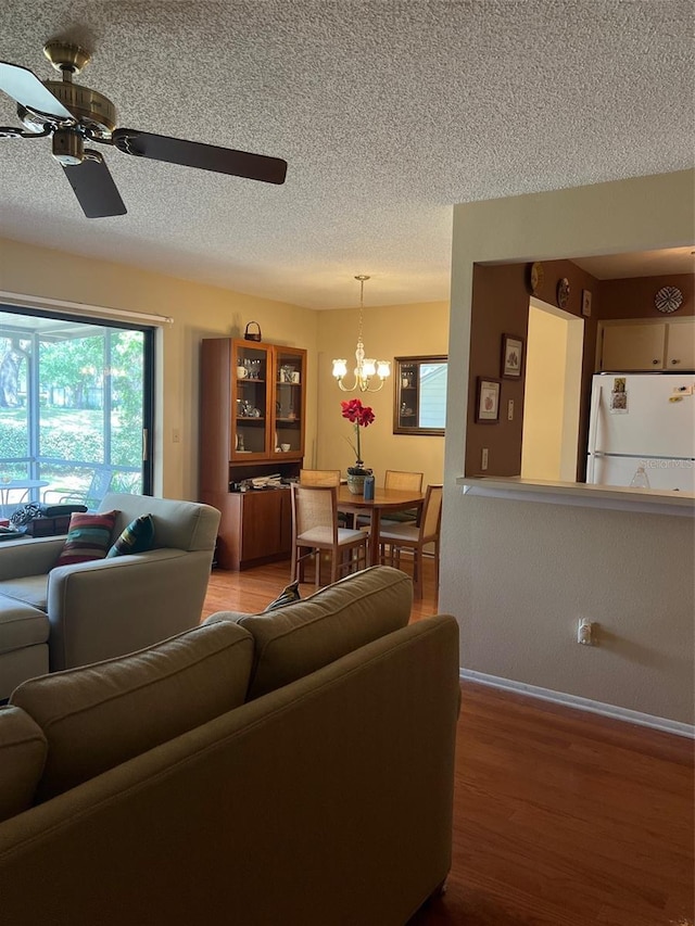 living room with light wood finished floors, a textured ceiling, ceiling fan with notable chandelier, and baseboards