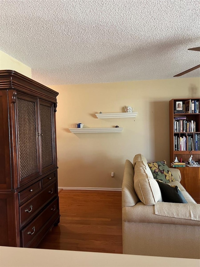 interior space featuring baseboards, ceiling fan, a textured ceiling, and wood finished floors