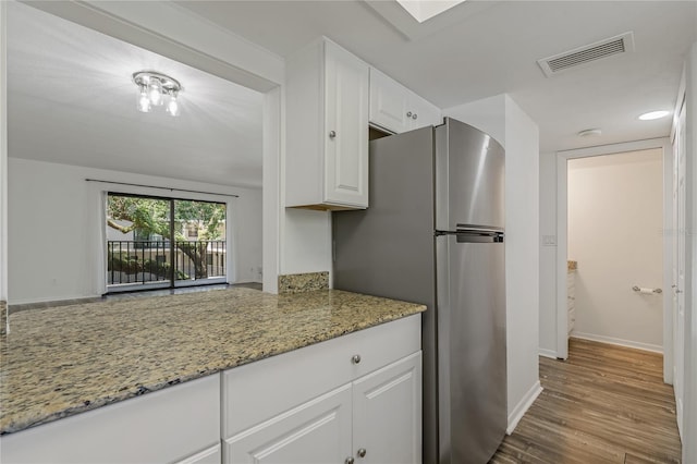 105 4th Ave NE Unit 220, Saint Petersburg, FL 33701 - kitchen with white cabinetry, freestanding refrigerator, light stone countertops, visible vents, and wood finished floors