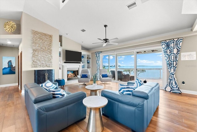 living room with a warm lit fireplace, wood finished floors, visible vents, and baseboards