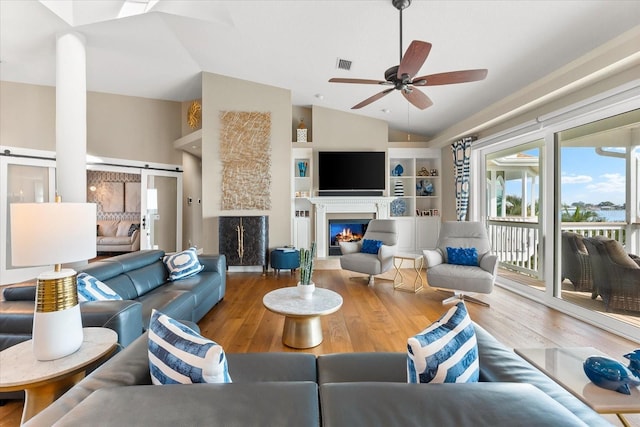 living room featuring vaulted ceiling, wood finished floors, a glass covered fireplace, ceiling fan, and visible vents