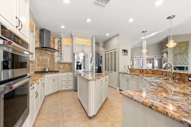kitchen with backsplash, visible vents, a sink, wall chimney exhaust hood, and appliances with stainless steel finishes