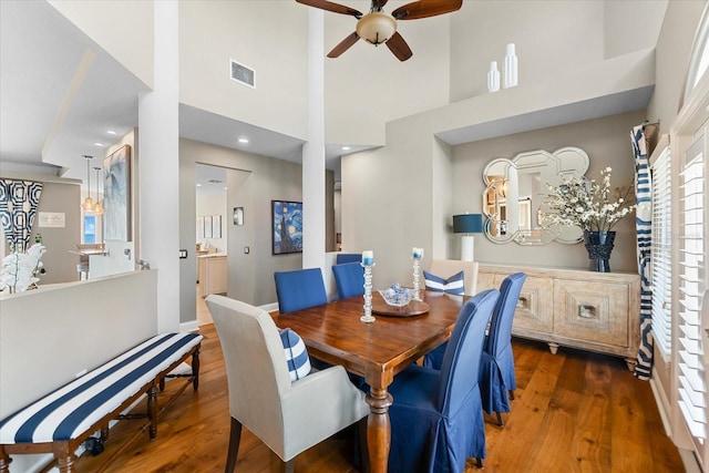 dining room featuring visible vents, a towering ceiling, a ceiling fan, and wood finished floors