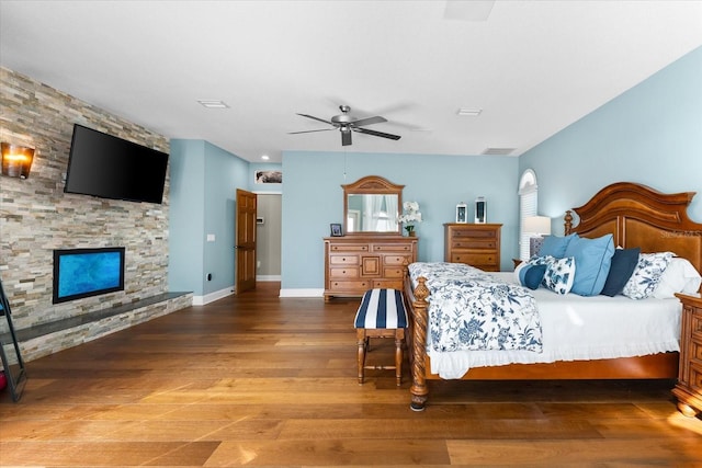 bedroom with a fireplace, wood finished floors, ceiling fan, and multiple windows