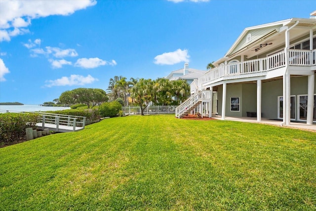 view of yard featuring a patio area, a water view, ceiling fan, fence, and stairway
