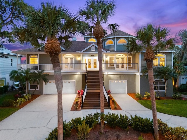 raised beach house featuring stairway, an attached garage, driveway, and french doors