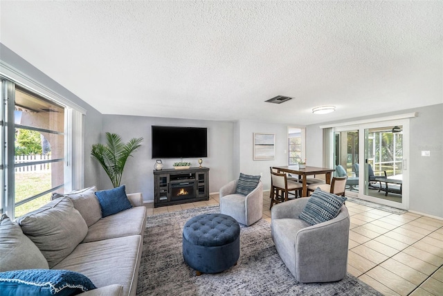 tiled living room featuring visible vents, a textured ceiling, and a warm lit fireplace