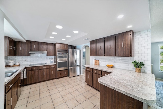 kitchen with a raised ceiling, arched walkways, light countertops, appliances with stainless steel finishes, and under cabinet range hood