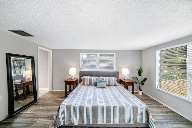 bedroom featuring visible vents, a textured ceiling, baseboards, and wood finished floors