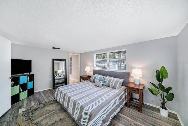 bedroom featuring visible vents, baseboards, wood finished floors, and a textured ceiling