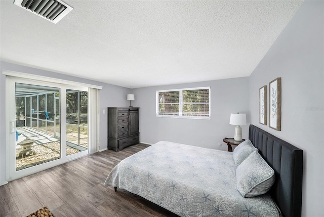 bedroom with a textured ceiling, visible vents, multiple windows, access to exterior, and wood finished floors