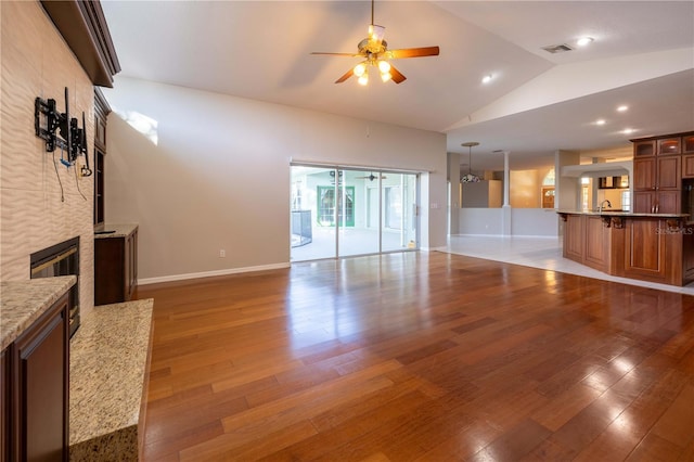 9159 Highland Ridge Way, Tampa, FL 33647 - unfurnished living room featuring baseboards, vaulted ceiling, a tiled fireplace, a ceiling fan, and wood finished floors