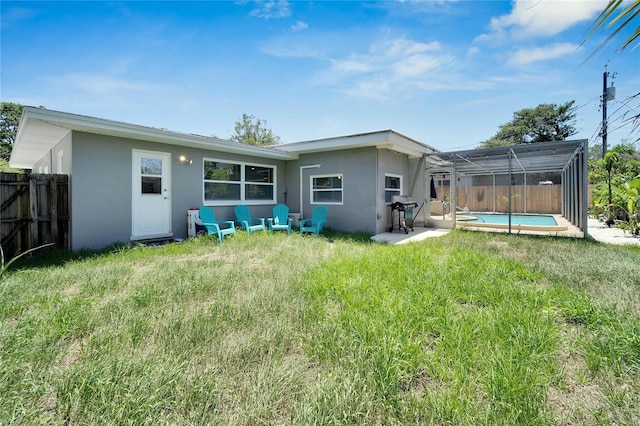 back of property featuring glass enclosure, fence, a yard, a fenced in pool, and stucco siding