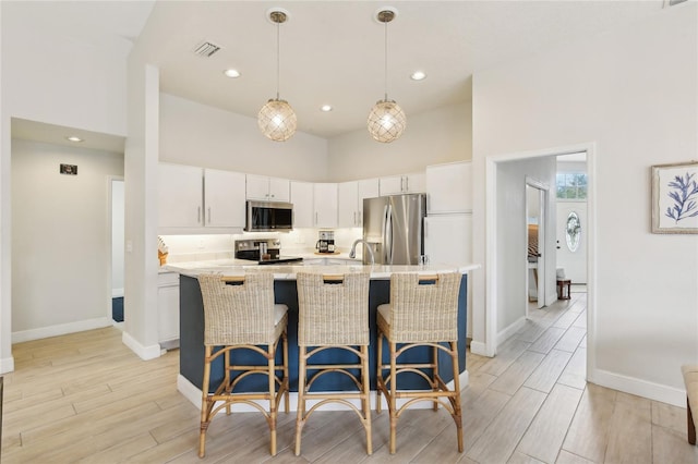kitchen with a sink, a breakfast bar, light wood-type flooring, baseboards, and appliances with stainless steel finishes