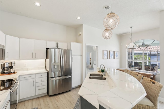 kitchen with white cabinets, a sink, a center island with sink, pendant lighting, and appliances with stainless steel finishes