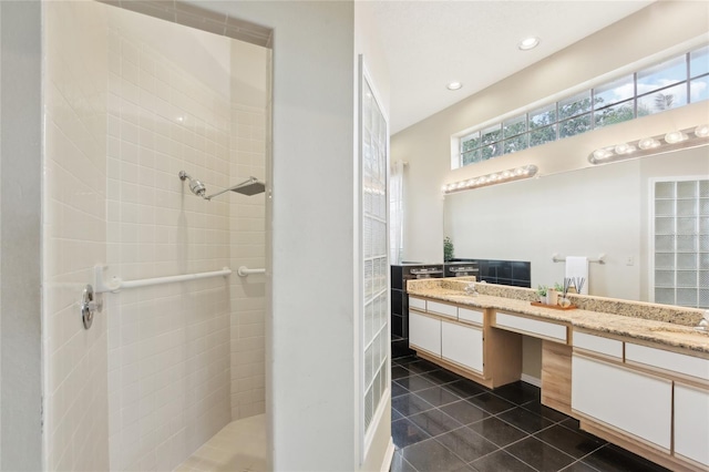 bathroom with a tile shower, tile patterned floors, double vanity, and a sink