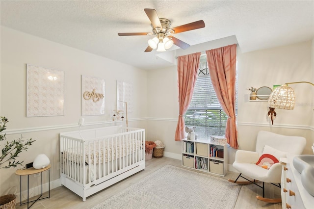 bedroom with a textured ceiling, baseboards, a ceiling fan, wood finished floors, and a nursery area