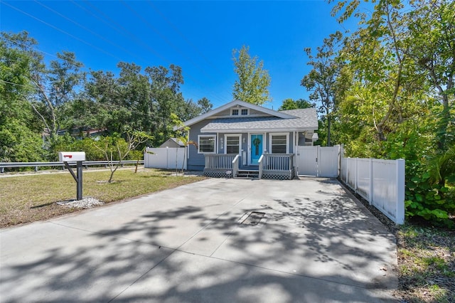 view of front of property with a gate, fence, driveway, covered porch, and a front yard