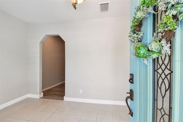 foyer with arched walkways, visible vents, baseboards, and light tile patterned floors