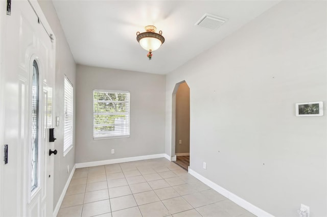 unfurnished room with baseboards, arched walkways, visible vents, and light tile patterned floors