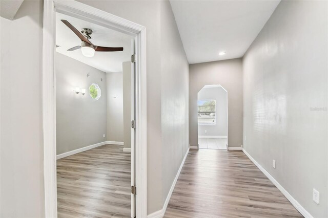 corridor featuring baseboards, arched walkways, light wood finished floors, and recessed lighting