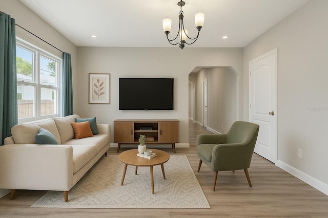 living area with arched walkways, baseboards, recessed lighting, an inviting chandelier, and light wood-style floors