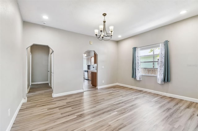 empty room with baseboards, a chandelier, arched walkways, and light wood-style floors