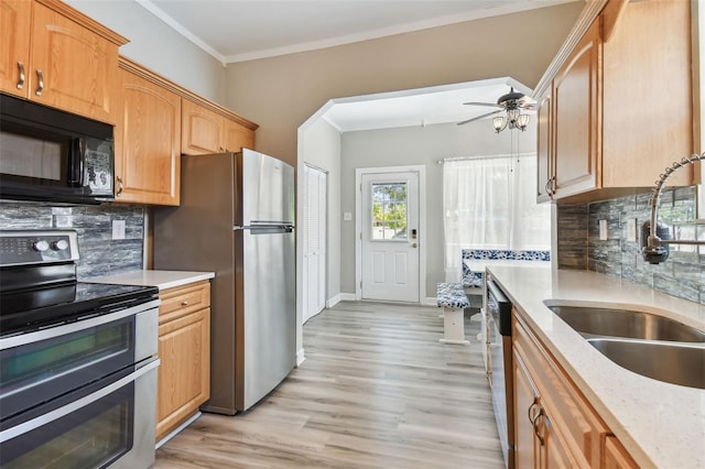 kitchen with a ceiling fan, a sink, stainless steel appliances, light wood-style flooring, and backsplash