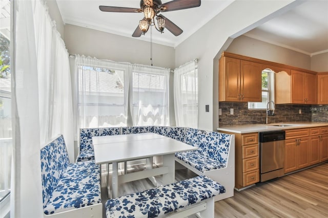 kitchen with light wood finished floors, a ceiling fan, stainless steel dishwasher, a sink, and decorative backsplash