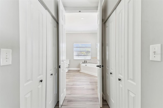 hall with light wood-style flooring, baseboards, and crown molding