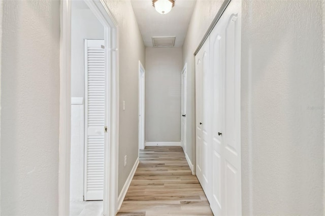 hallway featuring baseboards, visible vents, and light wood-style flooring