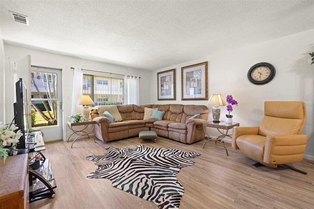 living area with a textured ceiling, wood finished floors, visible vents, and baseboards
