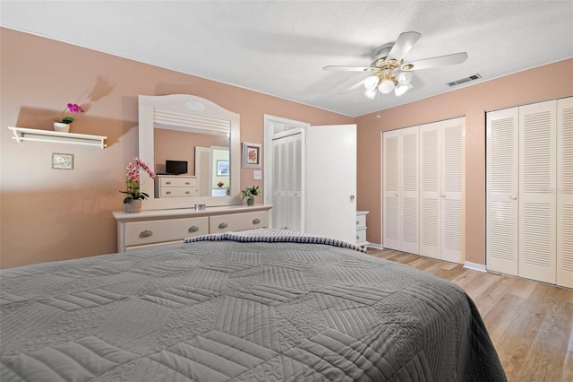 bedroom featuring baseboards, visible vents, light wood-style floors, ceiling fan, and multiple closets