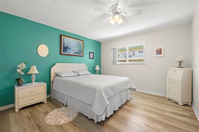bedroom featuring an accent wall, baseboards, a ceiling fan, and light wood-style flooring