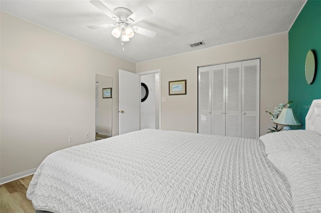 bedroom with a textured ceiling, visible vents, a ceiling fan, wood finished floors, and a closet