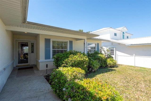 view of exterior entry with fence, stucco siding, and a lawn